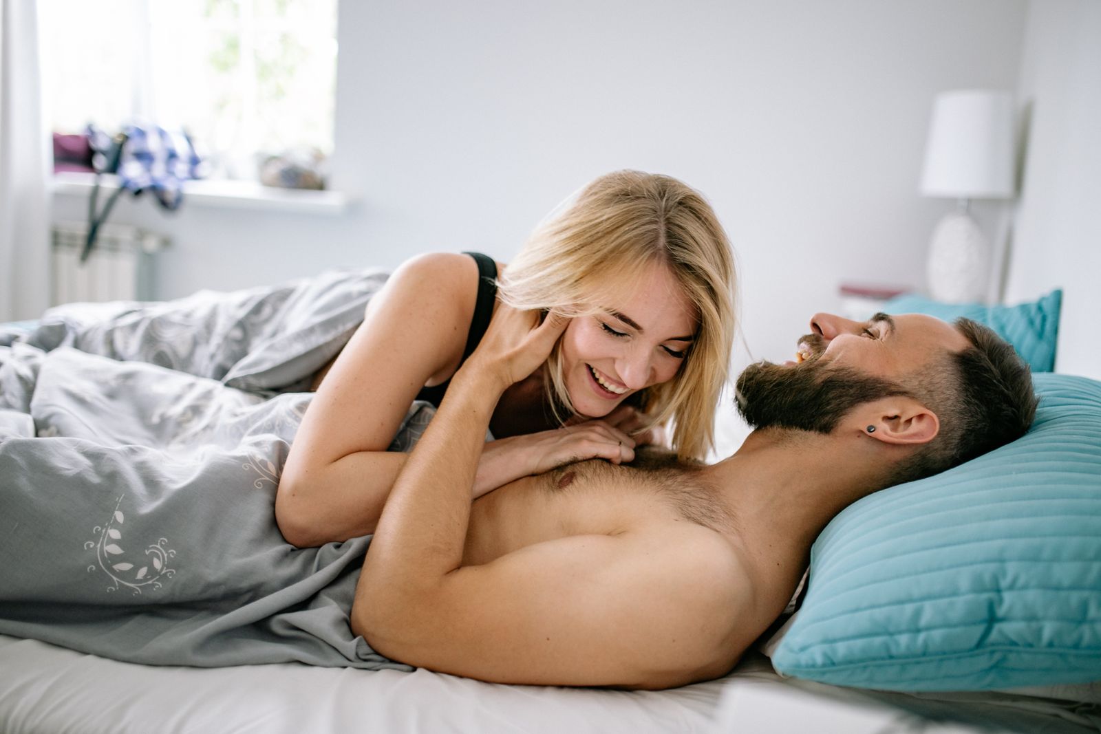 Two adults laughing together in bed in a sunlit room
