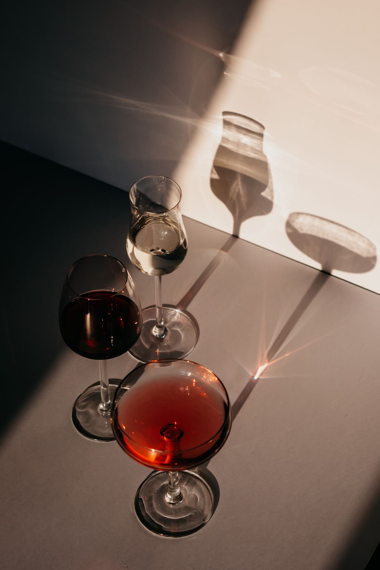 Three wine glasses with different drinks casting shadows