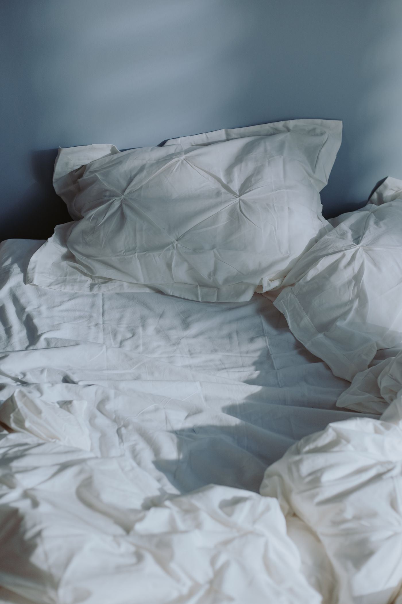 Unmade white linen bed in soft daylight, illustrating the morning after